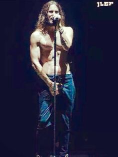 a shirtless man with long hair and no shirt on holding a microphone in front of him