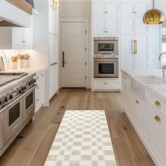 a kitchen with white cabinets and wood floors, an oven, sink, stove top and refrigerator