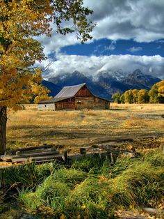 an old barn sits in the middle of a field with mountains in the back ground