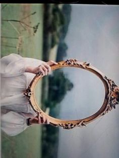 a woman in white dress holding up a gold mirror with ornate designs on it's sides