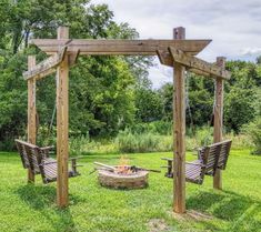 an outdoor fire pit in the middle of a grassy area with two chairs and a wooden arbor