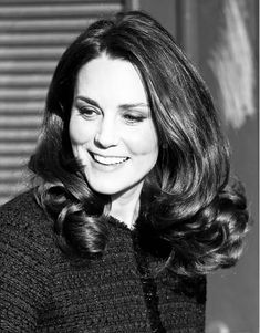 a black and white photo of a woman with long hair smiling at the camera, wearing a sweater