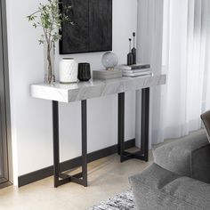 a white marble console table with black metal legs and a plant on top in a living room