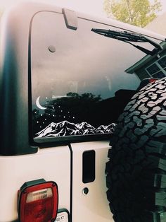 the back end of a white truck parked in front of a house with mountains and stars on it