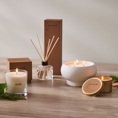 an assortment of candles, reeds and boxes on a wooden table with greenery