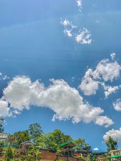 the sky is filled with white clouds and blue skies above some houses on top of a hill