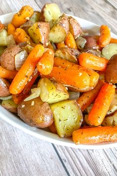 a white bowl filled with potatoes and carrots on top of a wooden table next to a fork