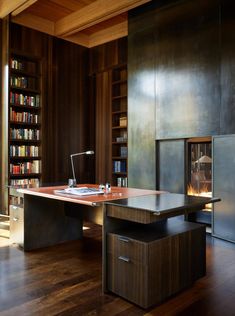 a desk with a laptop on it in front of a book shelf and fireplace area