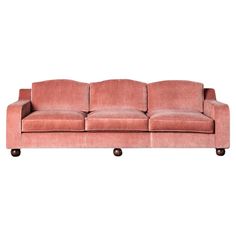 a pink velvet couch with wheels on the bottom and back legs, against a white background