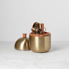 two brass pots with spoons and utensils in them on a marble surface