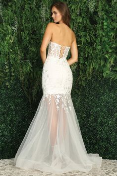 a woman in a white wedding dress standing next to a green wall with greenery