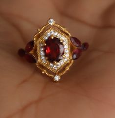 a woman's hand holding a ring with a red stone and white diamonds on it