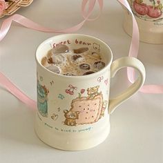 a cup filled with liquid next to some cookies and pink ribbon on a table top