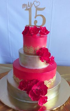 a three tiered cake with pink flowers on top and gold trim around the edges