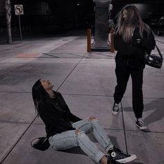 a woman sitting on the ground with her head up and another person standing in the background