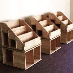 four wooden dollhouses lined up against a wall in a room with purple carpeted flooring