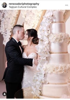 a bride and groom kissing in front of a wedding cake with white flowers on it