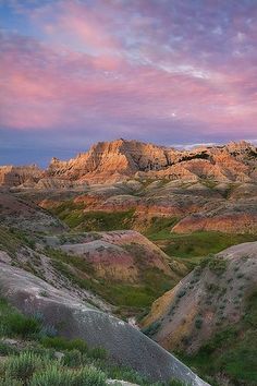 the mountains are covered in green grass and pink clouds at sunset, as seen from an overlook point