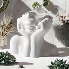 a white sculpture sitting on top of a table next to succulents