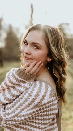 a beautiful young woman in a sweater posing for the camera with her hand on her chin