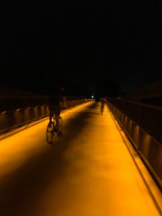 two bicyclists are riding on a bridge at night time with yellow lights