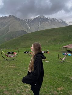 a woman standing on top of a grass covered field next to hammock chairs