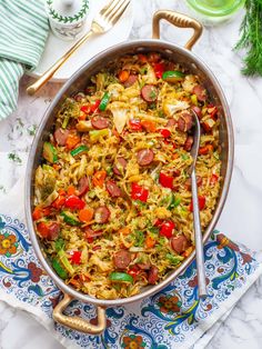 a large pan filled with rice, sausage and vegetables on top of a blue and white napkin