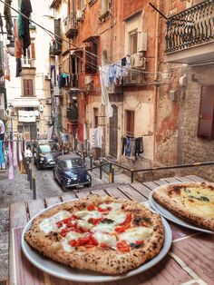 two pizzas are sitting on the table in front of an alleyway with parked cars