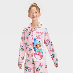 Your kid will stay cozy as they wind down for bed with this Squishmallows 2-Piece Coat Pajama Set in pink. This pack includes a long-sleeve sleep shirt in a front button-down style with allover Squishmallow prints along with the "Warm and Cozy" text plus pajama pants with an elastic waistband and the same Squishmallow prints. Made from jersey fabric, this classic-fit pajama set is a must-have addition to your kid's PJ wardrobe. Cozy Long Sleeve Sleepwear, Pink Sets For Sleepover In Winter, Pink Sets For Winter Sleepover, Pink Sleepover Set For Winter, Cozy Pink Sets For Sleepover, Pink Winter Sleepover Sets, Long Sleeve Character Print Sets For Sleepovers, Pink Winter Bedtime Sets, Pink Winter Sleepwear For Bedtime