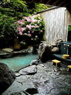 there is a small pool in the backyard next to some rocks and trees with pink flowers on it