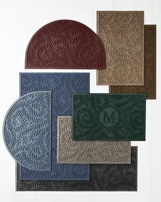 four bath mats with monogrammed leaves on them in various colors and sizes, all lined up against a white wall