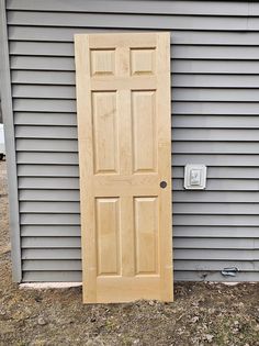 a wooden door sitting in front of a gray house next to a white light switch