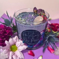 a candle that is sitting on a table next to some flowers and rocks with writing on it