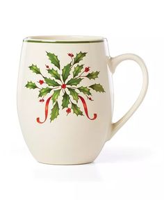 a white coffee cup with holly and red ribbon on the side, decorated with green leaves