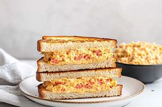 three slices of toasted bread with scrambled eggs on them and a bowl of macaroni and cheese in the background