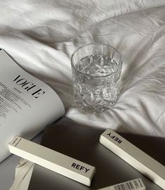 an open book sitting on top of a bed next to a glass filled with water