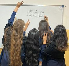 several girls writing on a white board with their hands in the air and pointing to it