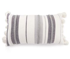 a gray and white striped pillow with tassels on the bottom, sitting on a white surface