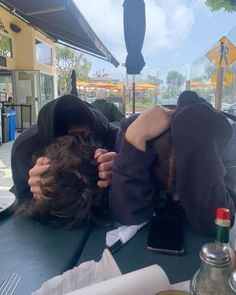 a person laying on top of a table covered in a black jacket and holding their head