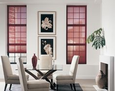 a dining room table with chairs and pictures on the wall behind it in front of two windows