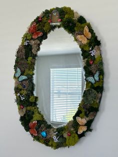 a mirror that has some plants and butterflies on it in the shape of a wreath