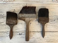 three paint brushes lined up next to each other on a white painted wood background with peeling paint