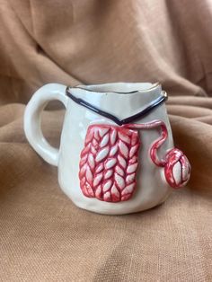 a white cup with red designs on it sitting on a brown cloth covered tablecloth