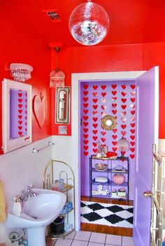 a bathroom decorated in pink and purple with hearts on the wall, mirror above the sink