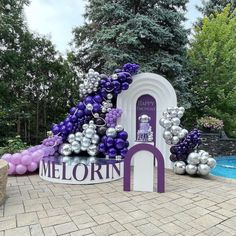 there is a purple and silver balloon arch next to the pool with balloons all over it