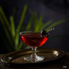 a glass filled with liquid sitting on top of a metal tray next to a green plant