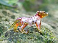 a small glass animal sitting on top of a mossy rock covered in lichen