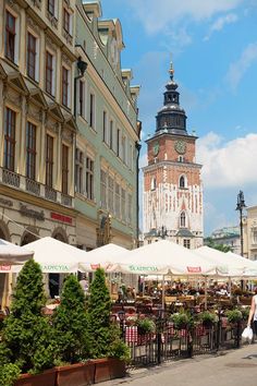 an outdoor market with tables and umbrellas in front of tall buildings on a sunny day