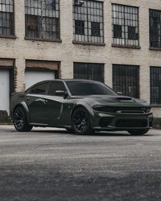 a green dodge charger parked in front of a brick building with lots of windows