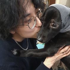 a woman in glasses kissing a small black dog